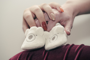 Photo de grossesse en lumière naturelle – parents tenant des chaussons sur le ventre de la future maman