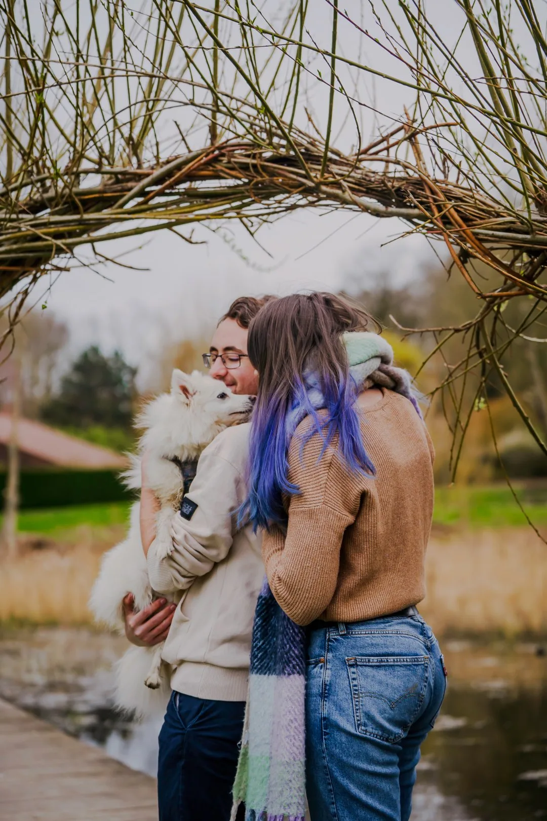 Couple et leur chien blanc rassemblés sous une arche en bois lors d’une séance photo lifestyle
